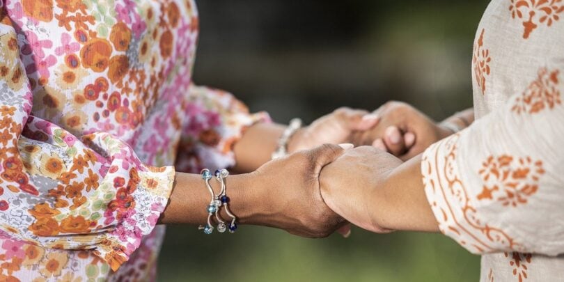 Zwei Menschen halten sich bei einer Schweigemeditation an den Händen, symbolisieren Verbundenheit und Achtsamkeit im Rahmen der Metta-Herzmeditation.