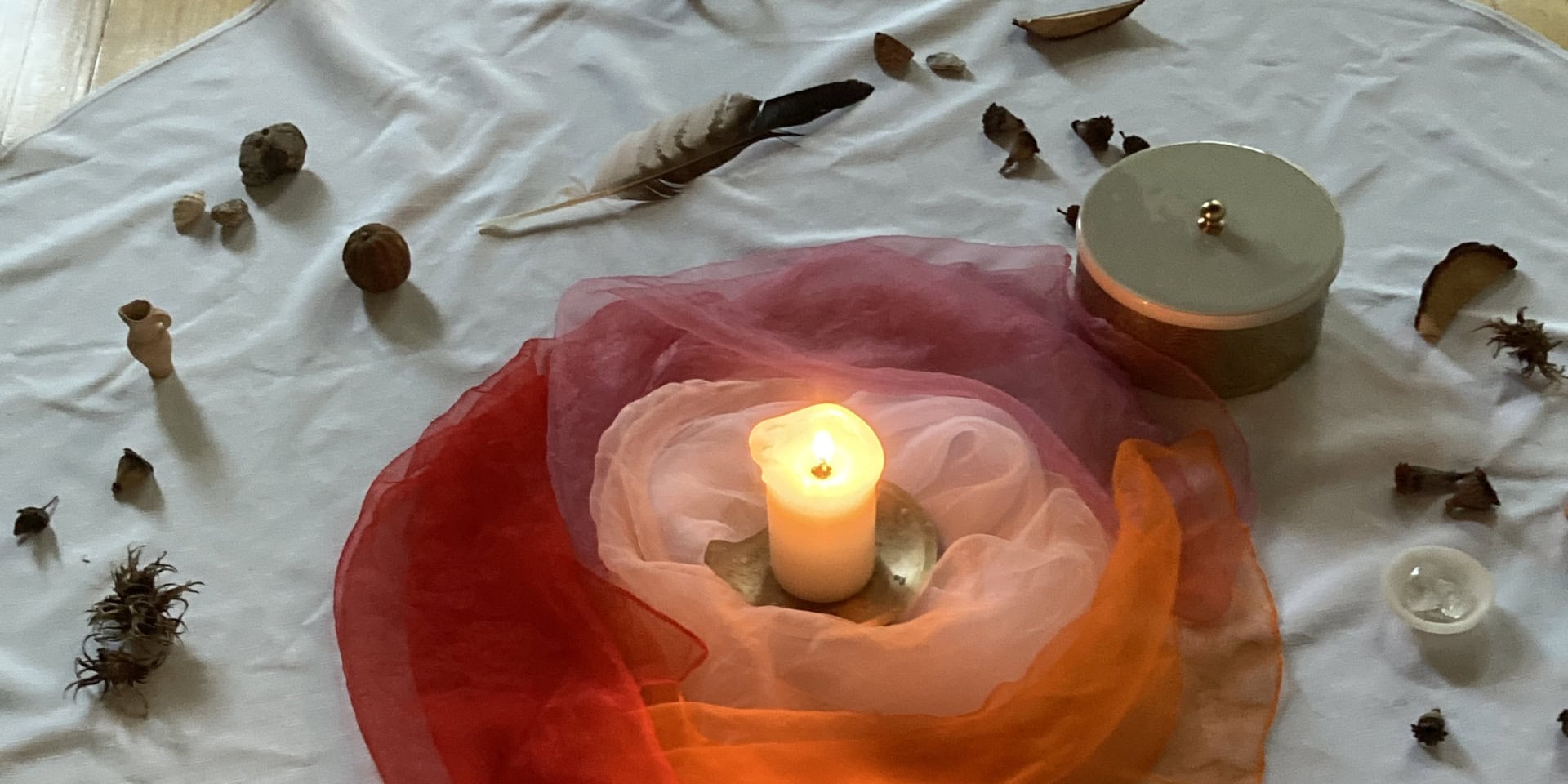 Ruhige Schweigemeditation mit Kerze, Federn und Naturmaterialien auf weißem Tuch, fördert Achtsamkeit und innere Ruhe.